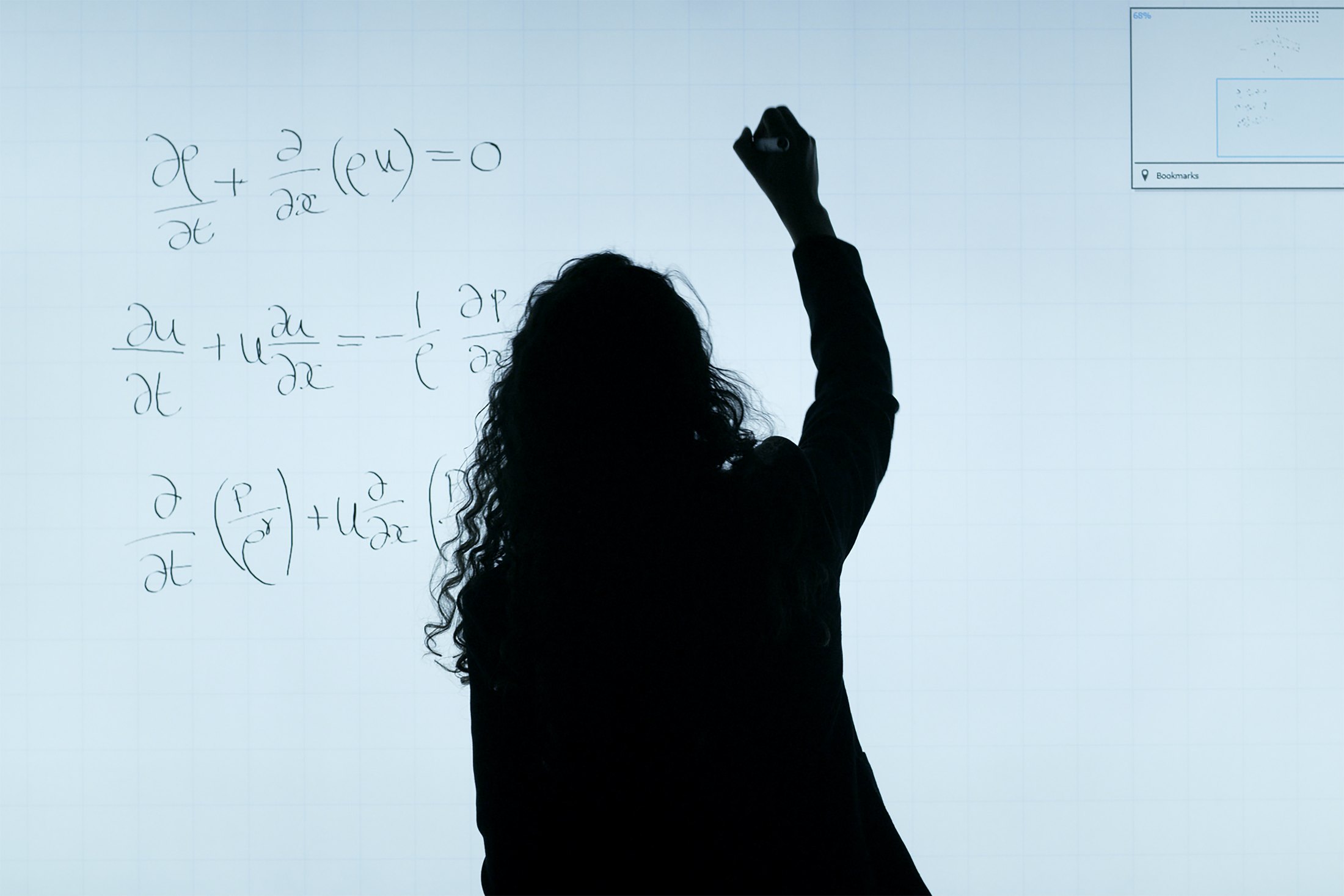 A photograph of a person writing fluid-dynamics equations on a glass board.